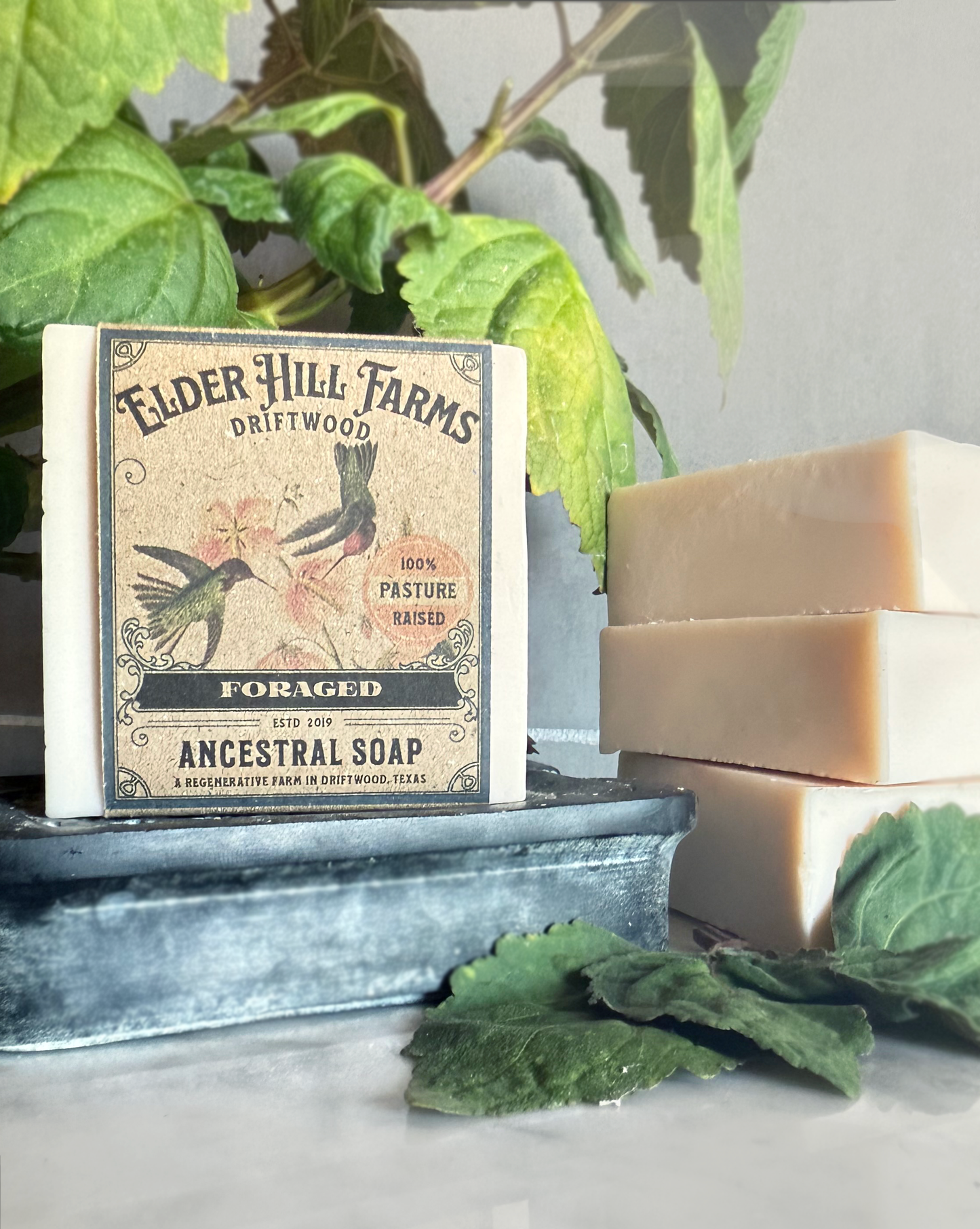 Bar of soap with a label on a metal tray surrounded by green patchouli leaves